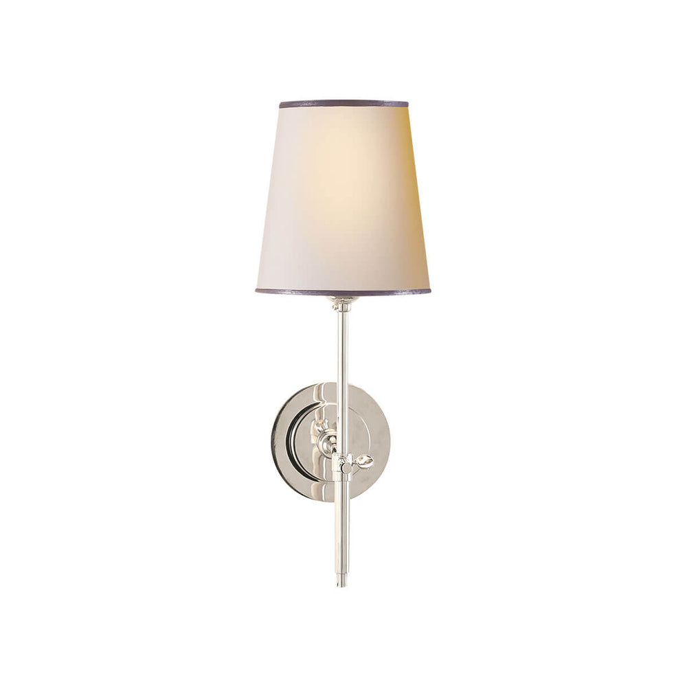 The Bryant Wall Sconce is a traditional sconce with a round backplate and simple arm with a polished nickel finish and a natural paper shade with a silver trim.