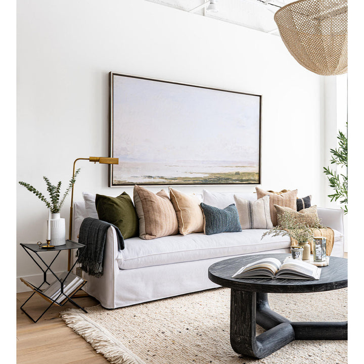 Lifestyle image featuring an extra long white sofa with textural throw pillows, coffee table, rug, and greenery in a neutral palette.