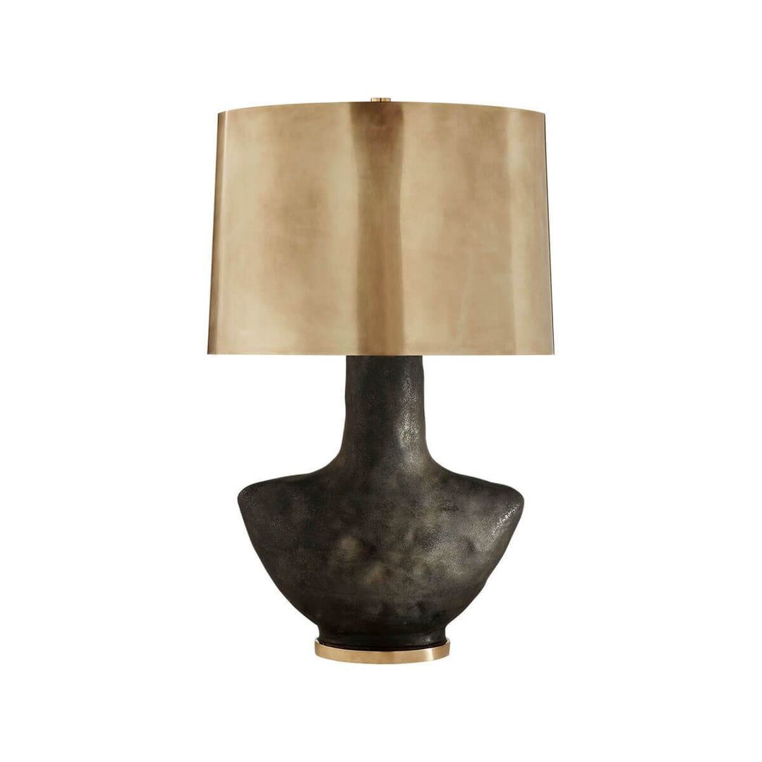 The Armato Table Lamp has a stained black metallic porcelain sculpture-like base and an oval antique brass shade. 