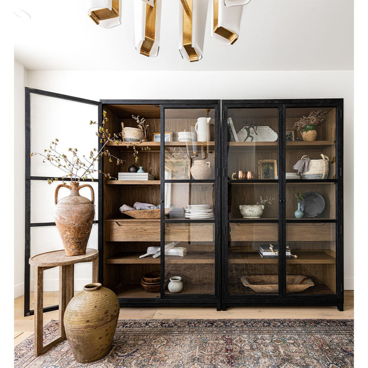 A rustic space with a black wood and glass cabinet showcasing pottery, serve wear,  and decor.