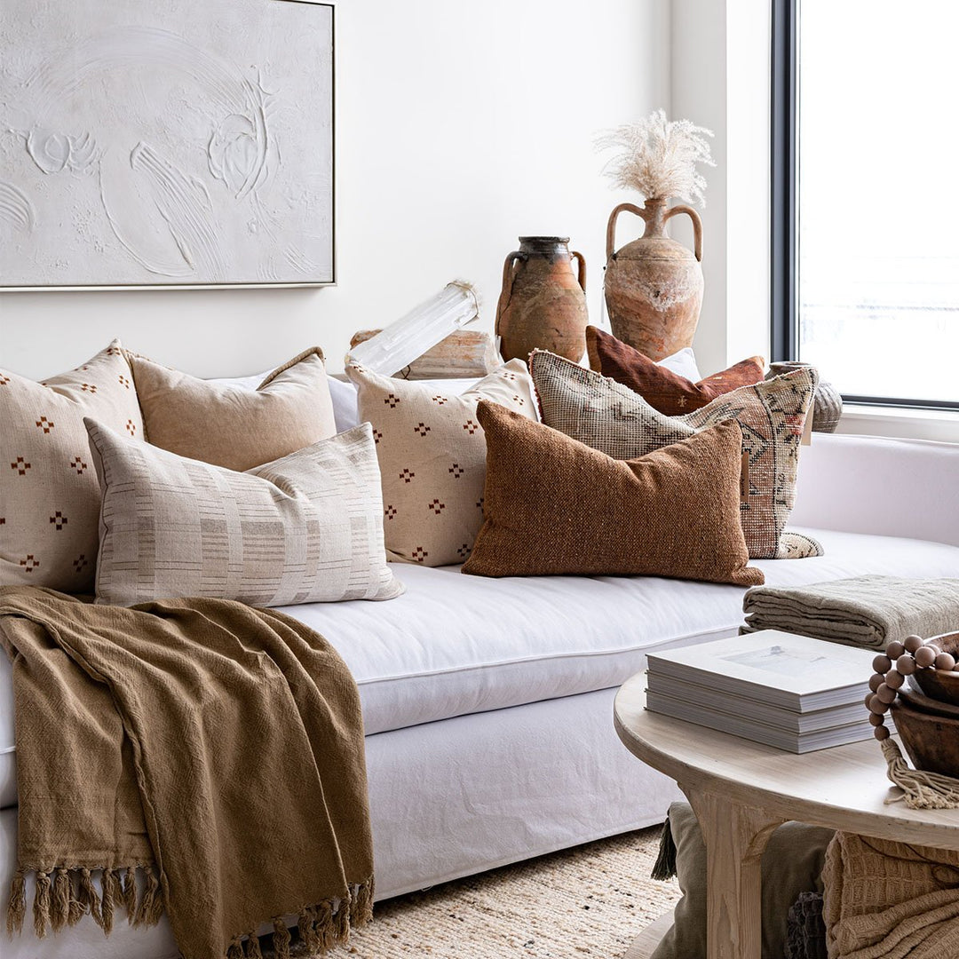 A neutral-toned living room featuring a white sofa, with terracotta and blush toned pillows, and vintage pottery..