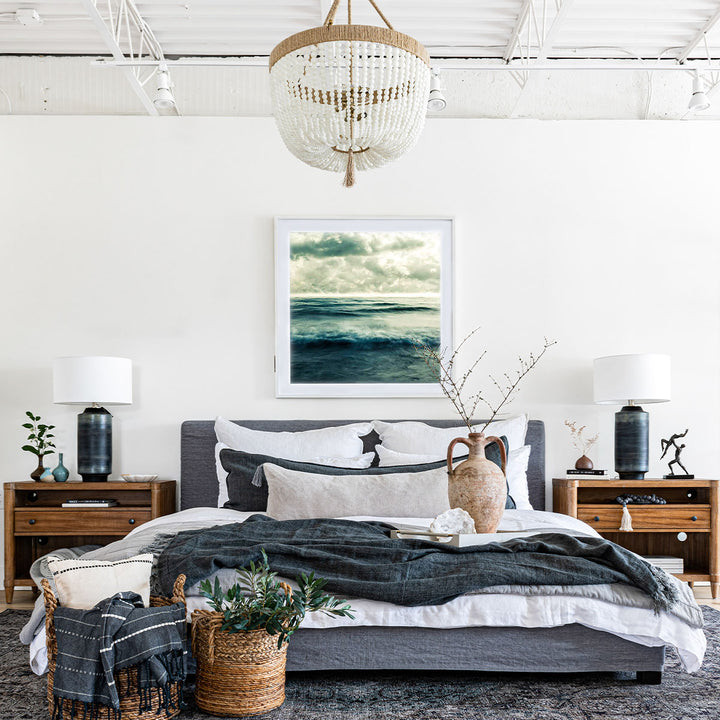 Modern bedroom set up with grey and dark tones with textural throw blankets and pillows, featuring a beaded chandelier.
