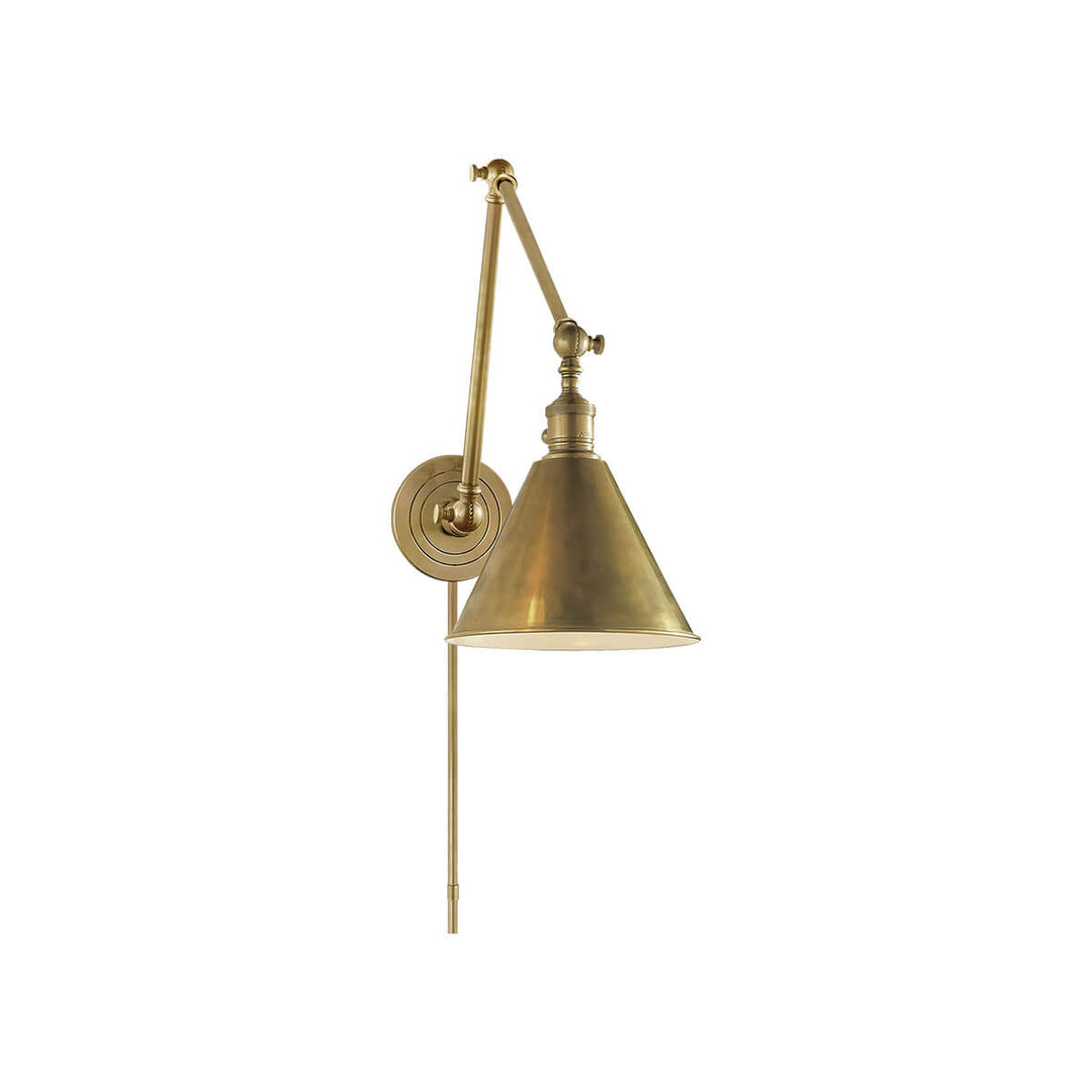 The Boston Double Arm Wall Light is an adjustable wall sconce with a round backplate in a hand-rubbed antique brass finish.