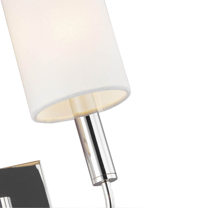 Closeup of the cylindrical white linen shade and slender polished nickel arm on the modern wall sconce.