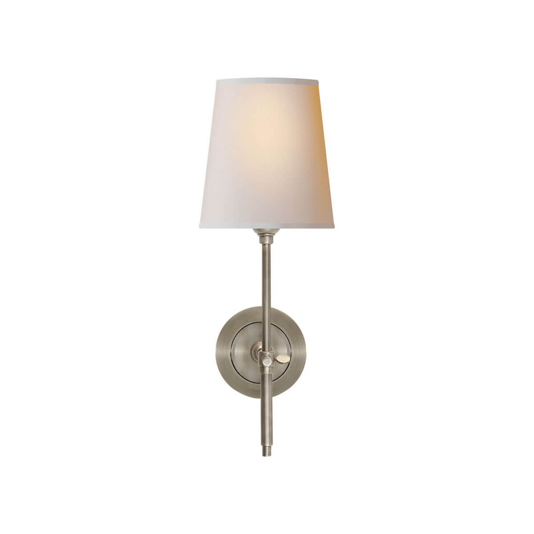 The Bryant Wall Sconce is a traditional sconce with a round backplate and simple arm with an antique nickel finish and a natural paper shade.
