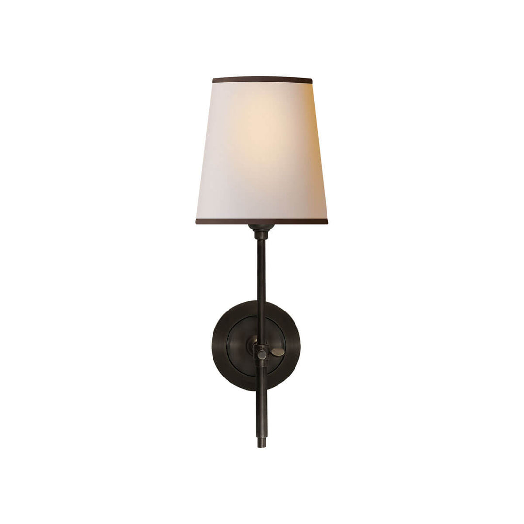 The Bryant Wall Sconce is a traditional sconce with a round backplate and simple arm with a bronze finish and a natural paper shade with a black trim.