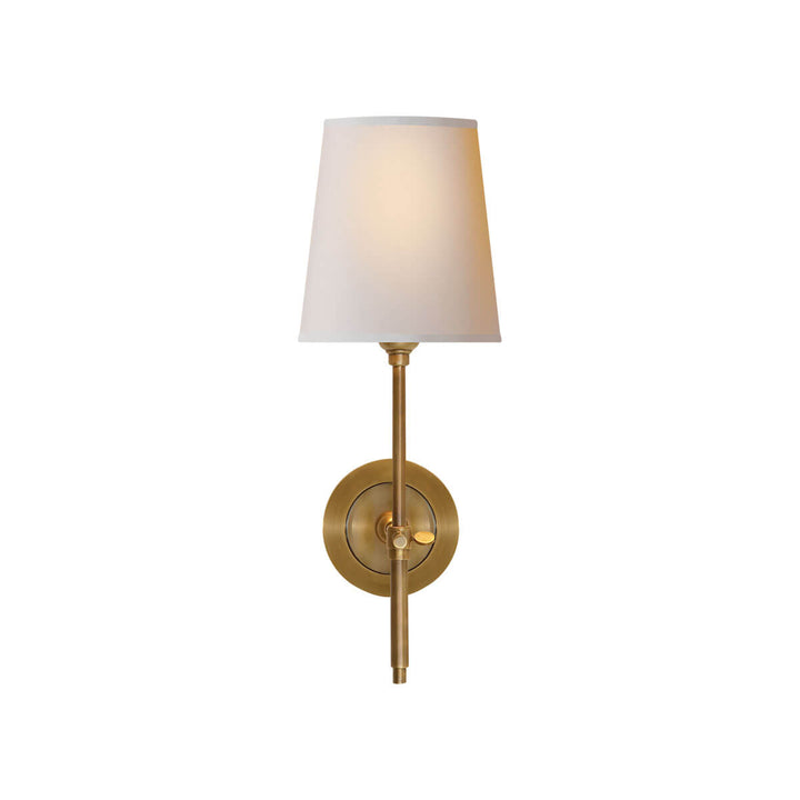 The Bryant Wall Sconce is a traditional sconce with a round backplate and simple arm with a hand rubbed antique brass finish and a natural paper shade.