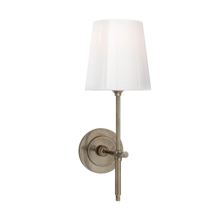 The Bryant Wall Sconce is a traditional sconce with a round backplate and simple arm with an antique nickel finish and a white glass shade.