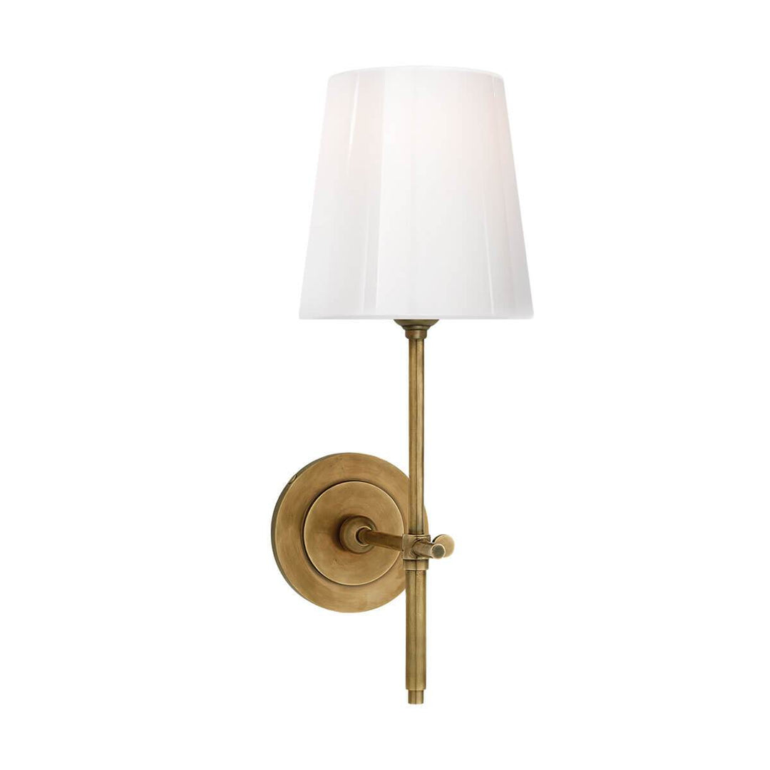The Bryant Wall Sconce is a traditional sconce with a round backplate and simple arm with a hand rubbed antique brass finish and a white glass shade.