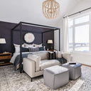 Modern grey and neutral toned bedroom with canopy bed, sofa, and large ottomans.
