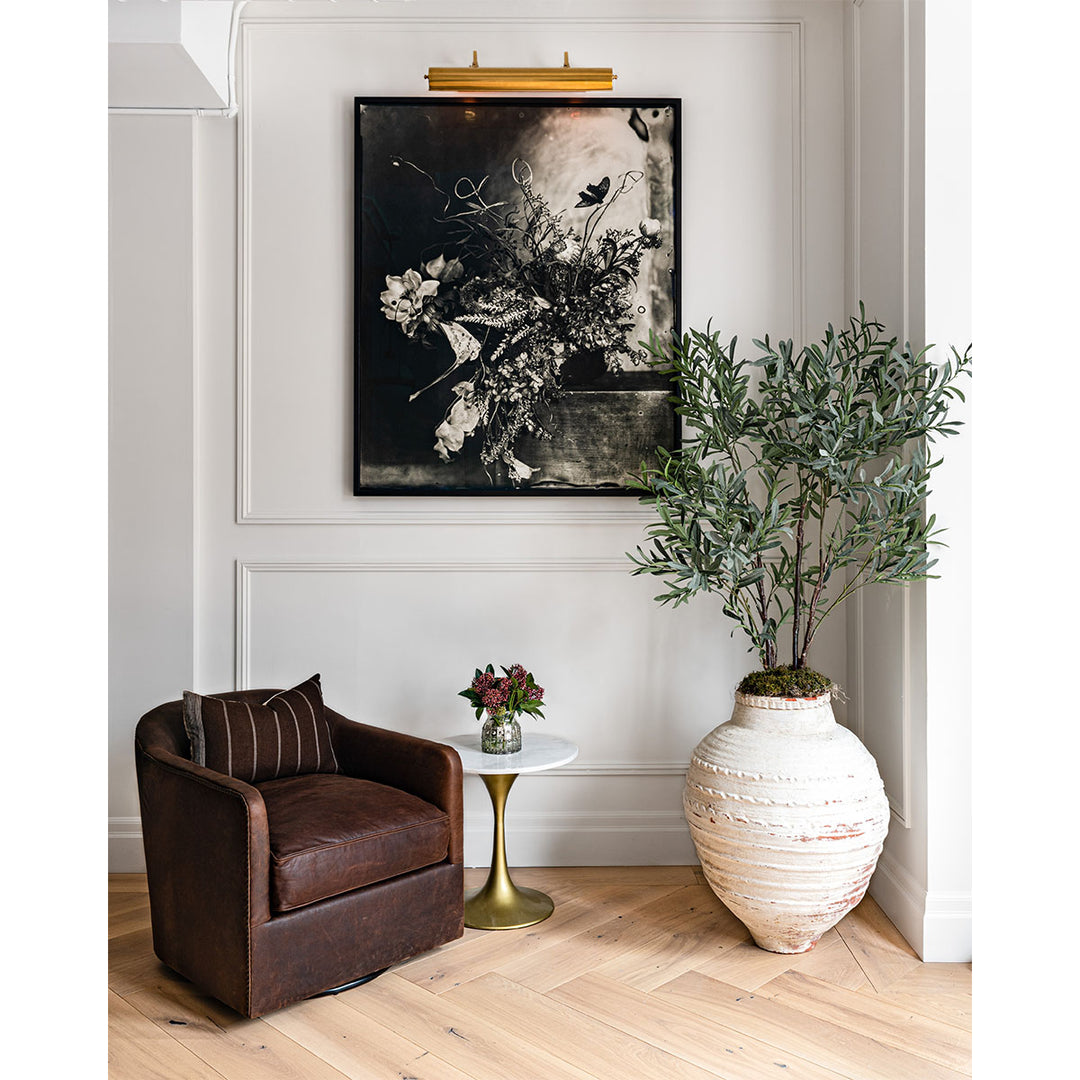 Small seating area with dramatic art and natural brass picture light, and large olive tree.