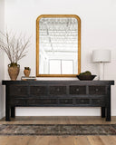 Faux forsythia in vintage jar on console table beneath large gold frames mirror.