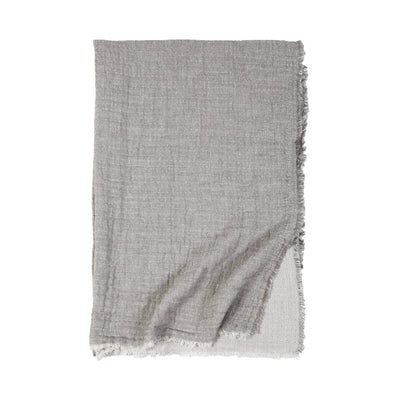 The Trento Oversized Throw is a light grey and cream stonewashed cotton and linen throw with frayed edges and a soft gauzy weave.
