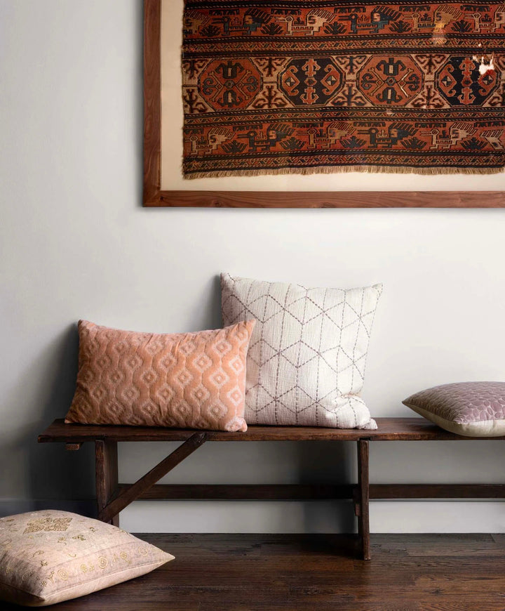 Throw pillows on a bench under a vintage rug.
