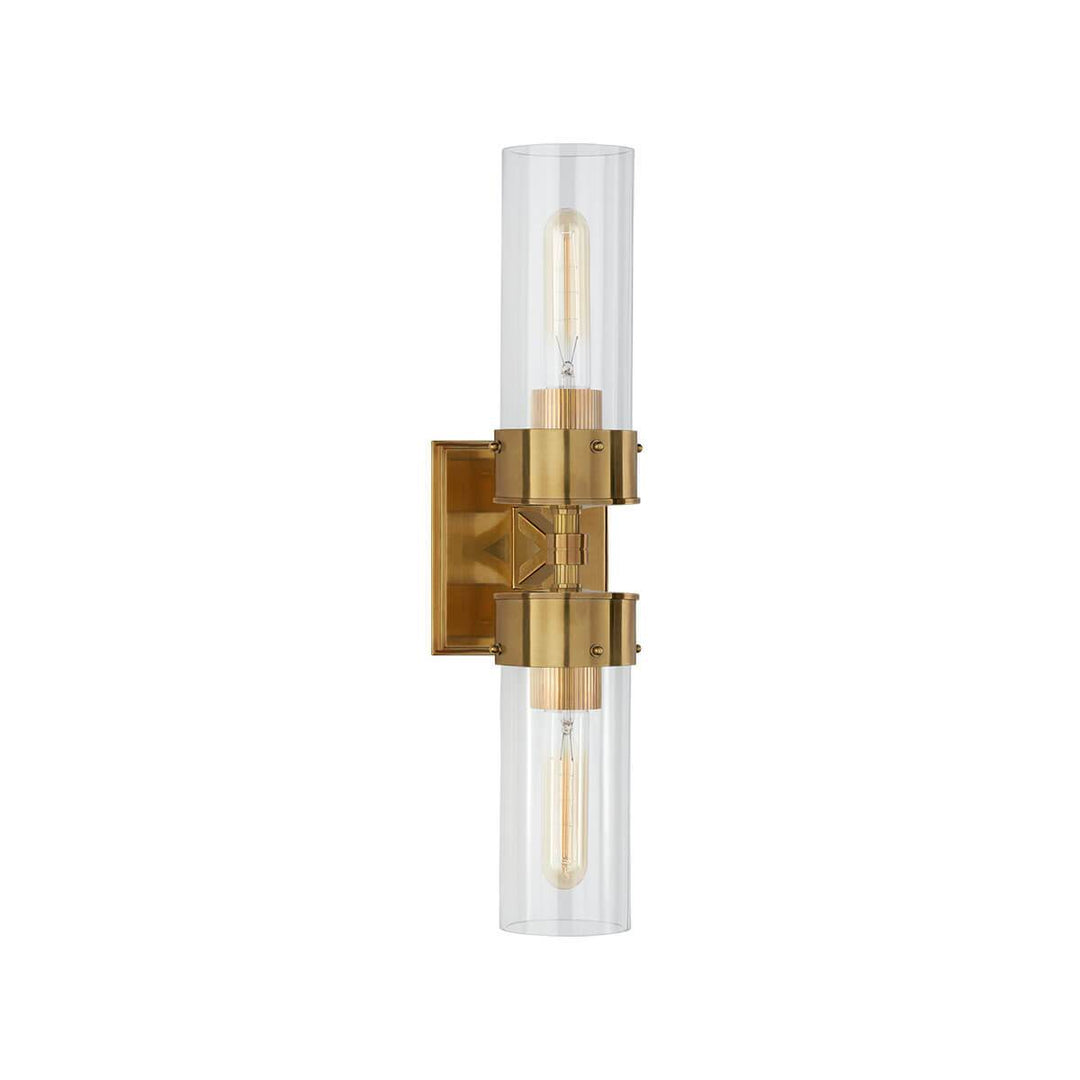 The Marais Double Wall Sconce has two clear glass, cylindrical lamp shades and a hand rubbed antique brass, square backplate and hardware.