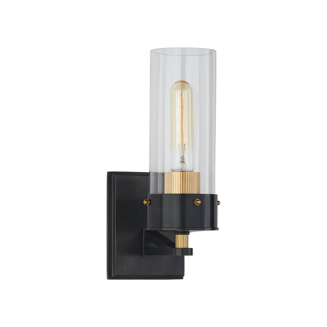 The Marais Wall Sconce has a bronze square backplate with antique brass details and covered bolts and a clear glass cylindrical shade.