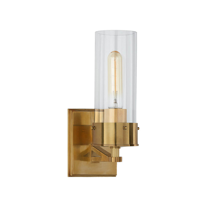 The Marais Wall Sconce has a hand-rubbed antique brass square backplate and covered bolts and a clear glass cylindrical shade.
