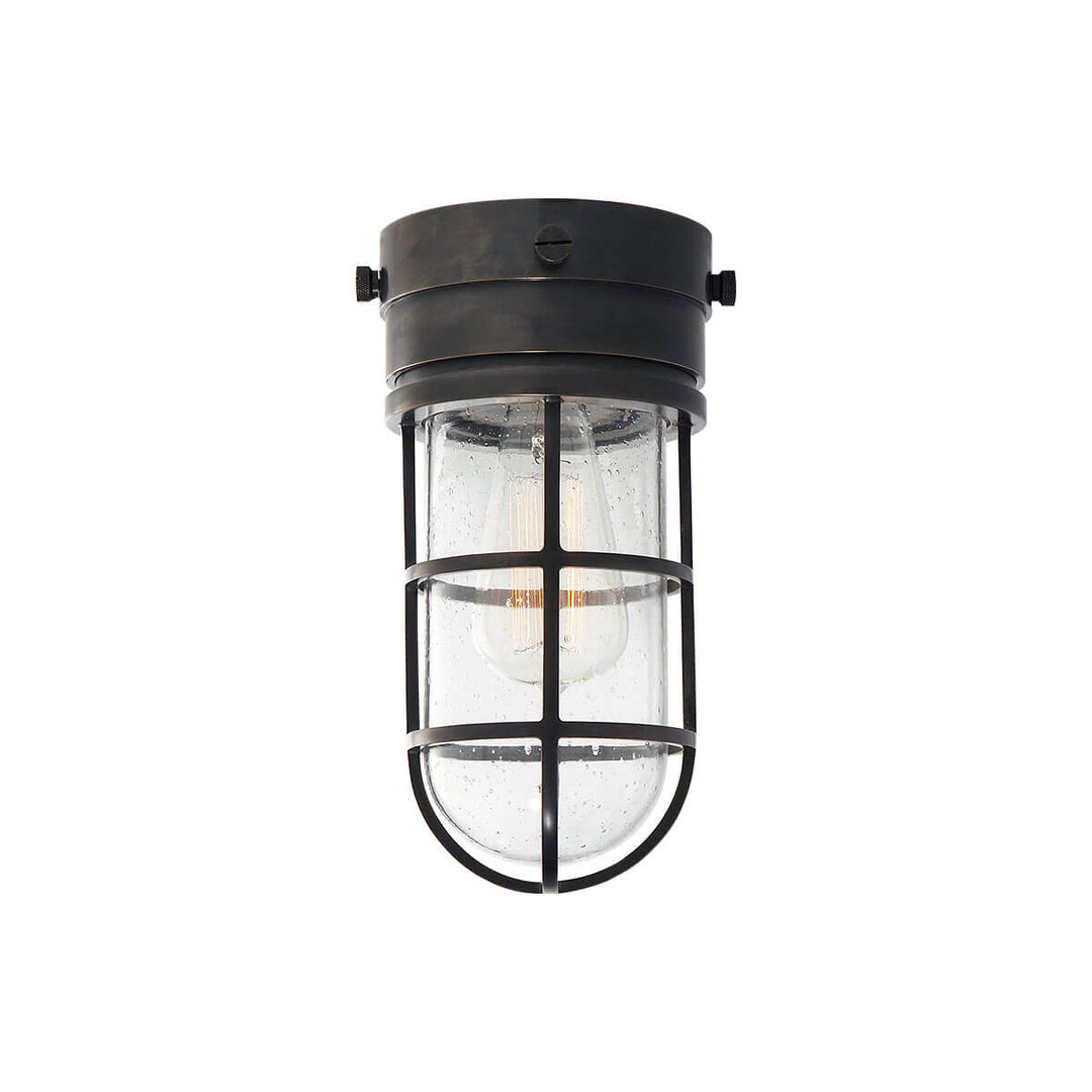 The Marine Flush Mount is an industrial looking caged light with a bronze base and a seeded glass shade.