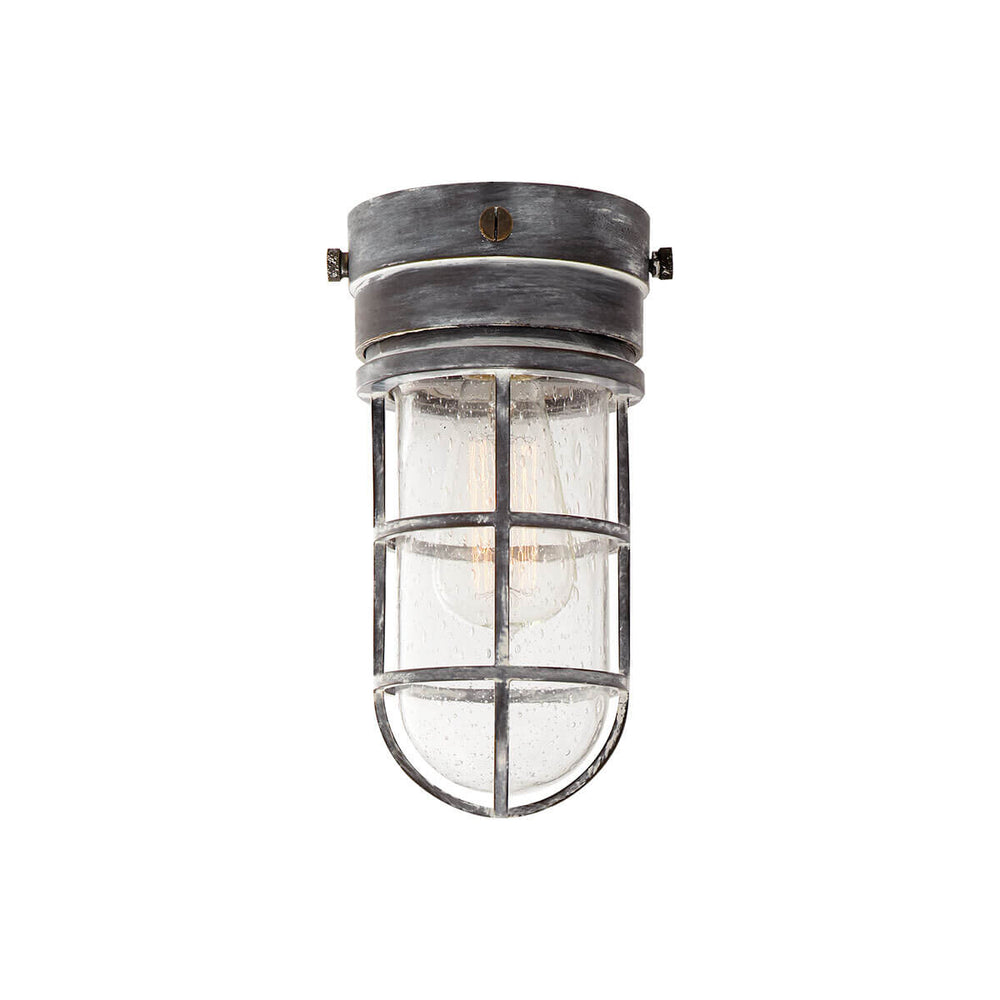 The Marine Flush Mount is an industrial looking caged light with a weathered zinc base and a seeded glass shade.