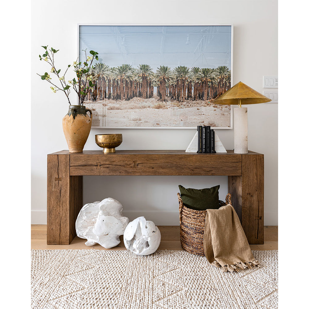 Photo of console table with large palm tree photograph, vintage pottery, textural rug, and marble with gold table lamp.