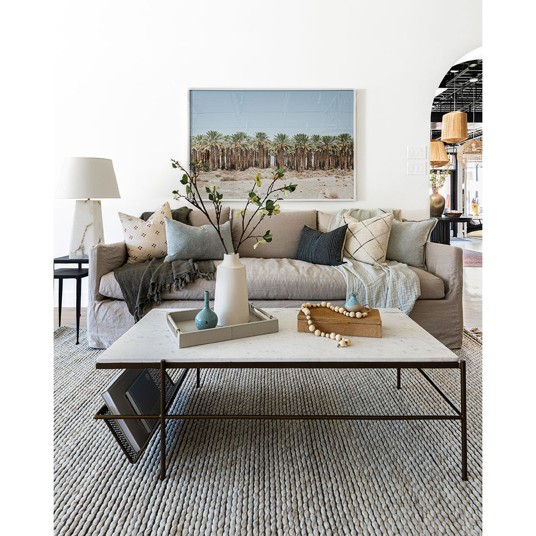 Lifestyle image of beige, slim, modern shaped sofa. Styled with side nesting tables, table lamp, marble coffee table and textural throw pillows.