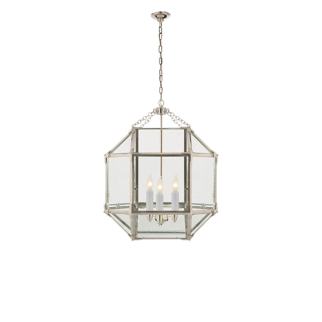 The Bruggen Medium Lantern has three candelabra lights in the middle of a polished nickel cage-like frame with visible joints and clear glass panels.
