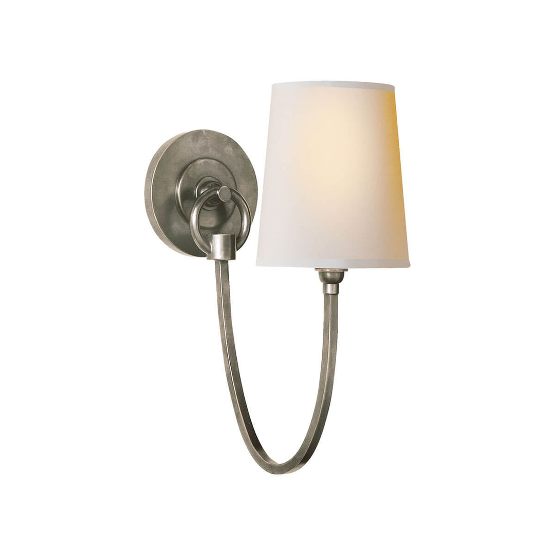 The Reed Wall Sconce has a natural paper shade and an antique nickel hooked arm and round backplate.