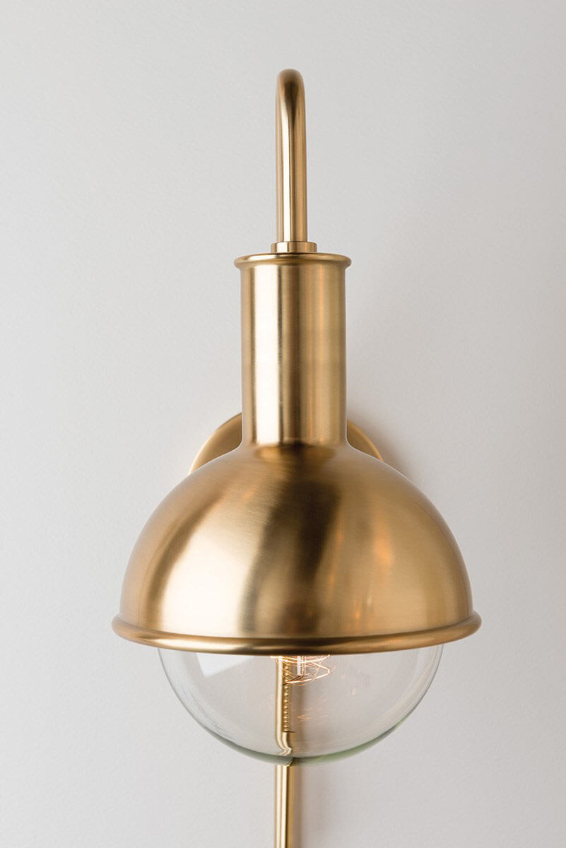 Aged brass modern looking wall sconce with a round glass bulb.