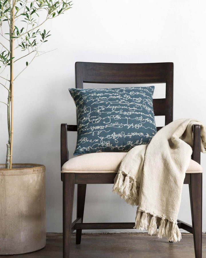 Taupe throw blanket with a fringe edge on a modern armchair.