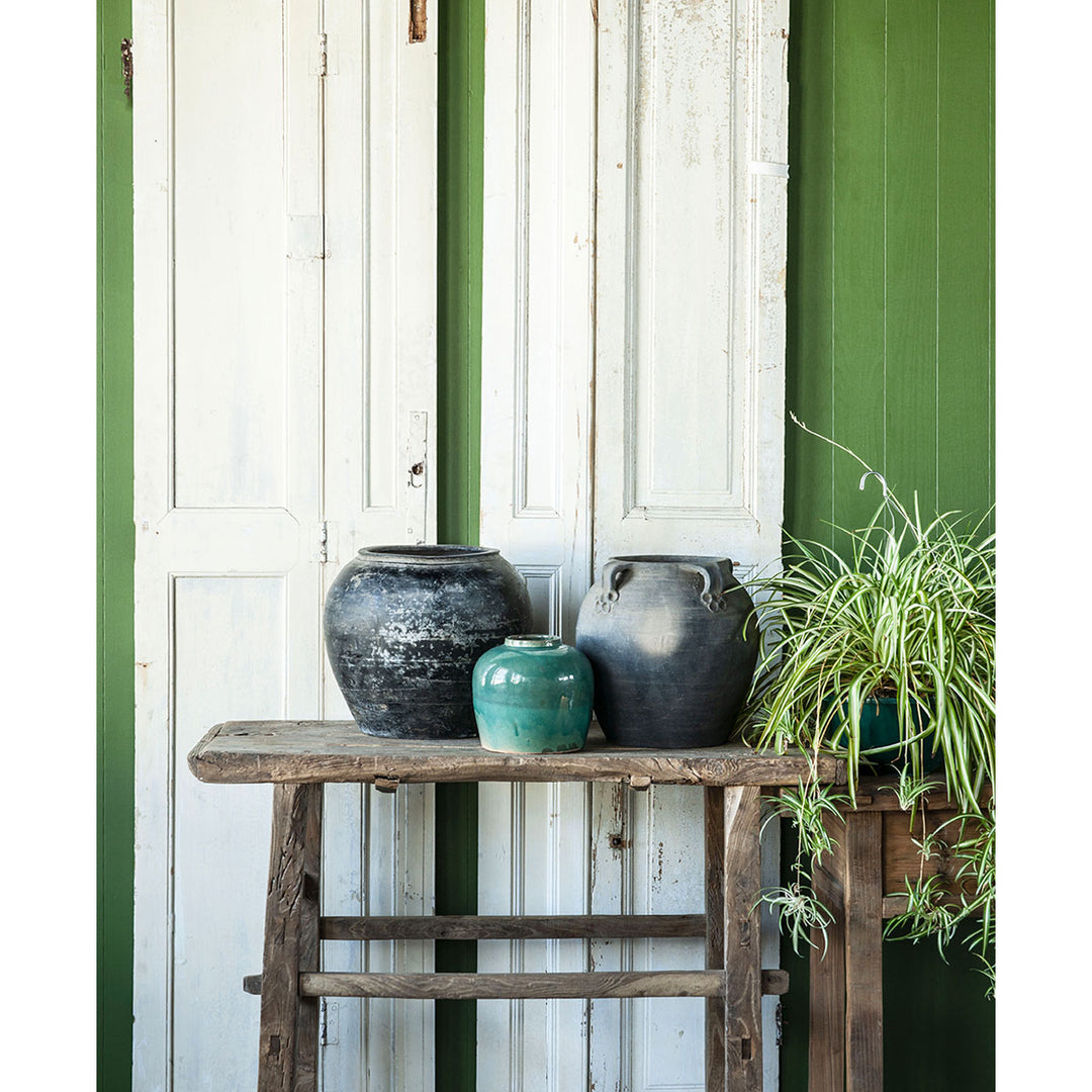 Lifestyle image featuring a rustic wooden table holding three antique vases and pots.