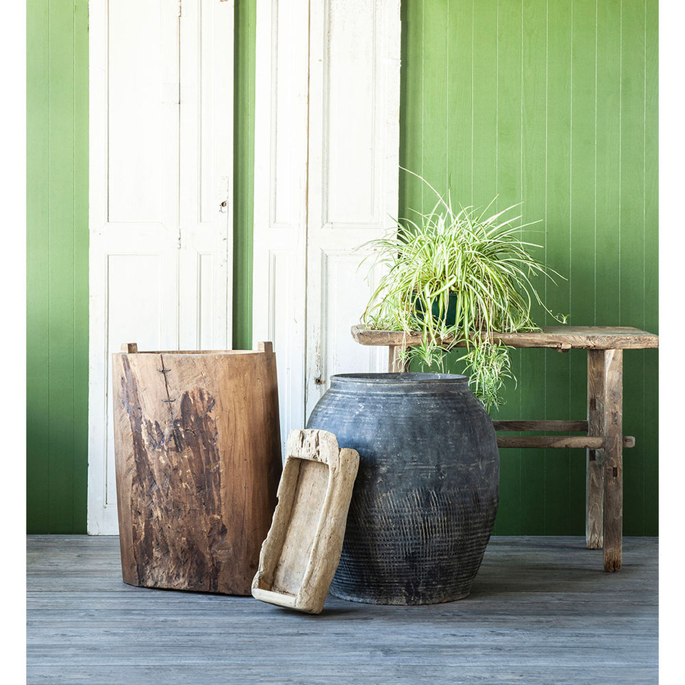 Lifestyle image of antique water pot styled outdoors with wooden elements and plants.
