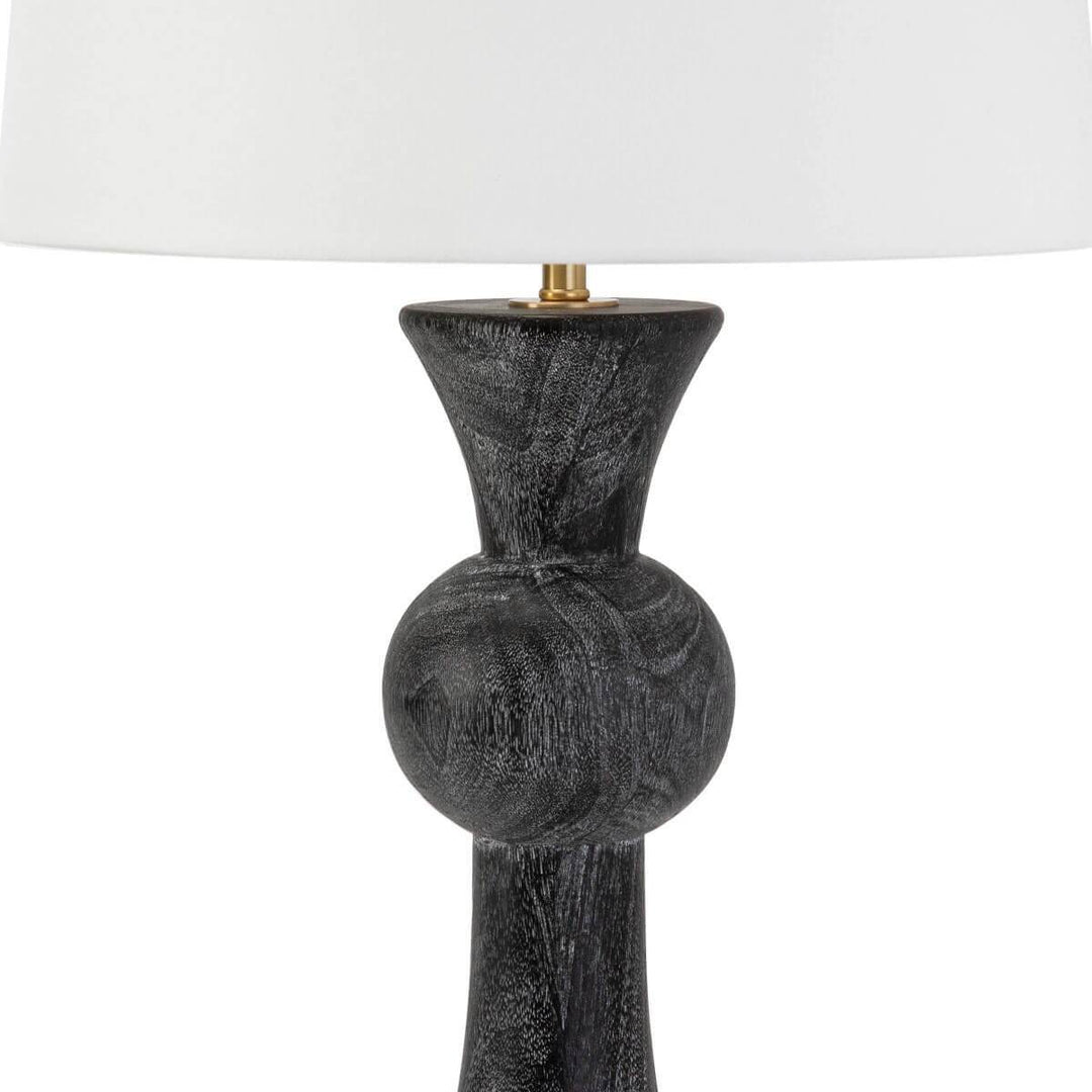 Modern table lamp with a carved oak wood base in a black finish with a white lamp shade and brass hardware.