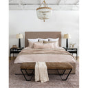 A lifestyle image of the Villa Bed in a king size. Styled with a leather bench, blush-toned antique rug, beaded chandelier, Black night stands, and blush pillows. Custom upholstery in a brown natural tone.