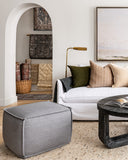 Lifestyle image of bohemian living room furniture with white sofa and large grey ottoman.