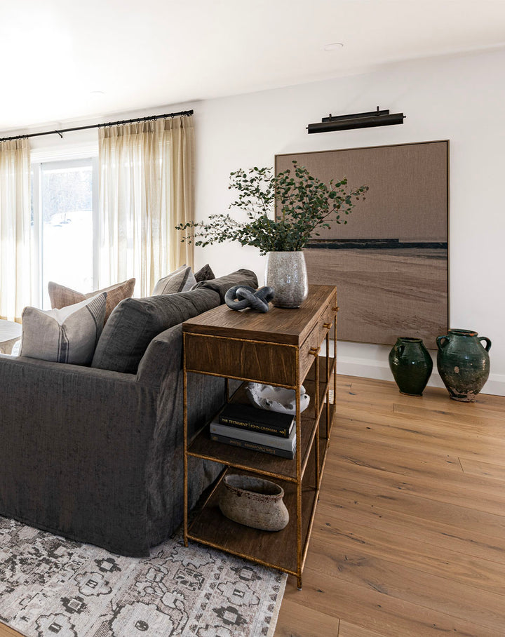 A neutral piece of artwork depicting a sandy beach in neutral colours with a modern, coastal vibe. Hanging in a cozy living room with a styled console and vintage accesories.