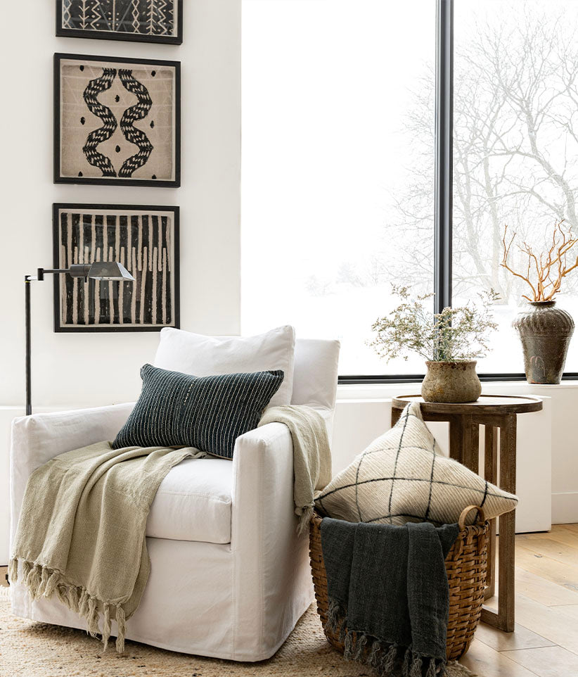 Woven tribal art showcased above white upholstered lounge chair with throw blankets and pillows, with a snowy winter scene outside.