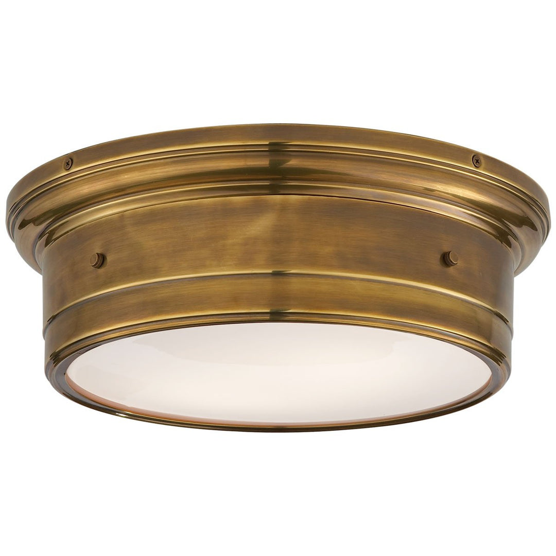 The Siena Flush Mount in Large has a simple drum shape in a hand-rubbed antique brass finish with covered bolt details and a white glass diffuser.
